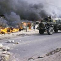 An armoured vehicle patrols past burning houses in the KTC squatter community camp
